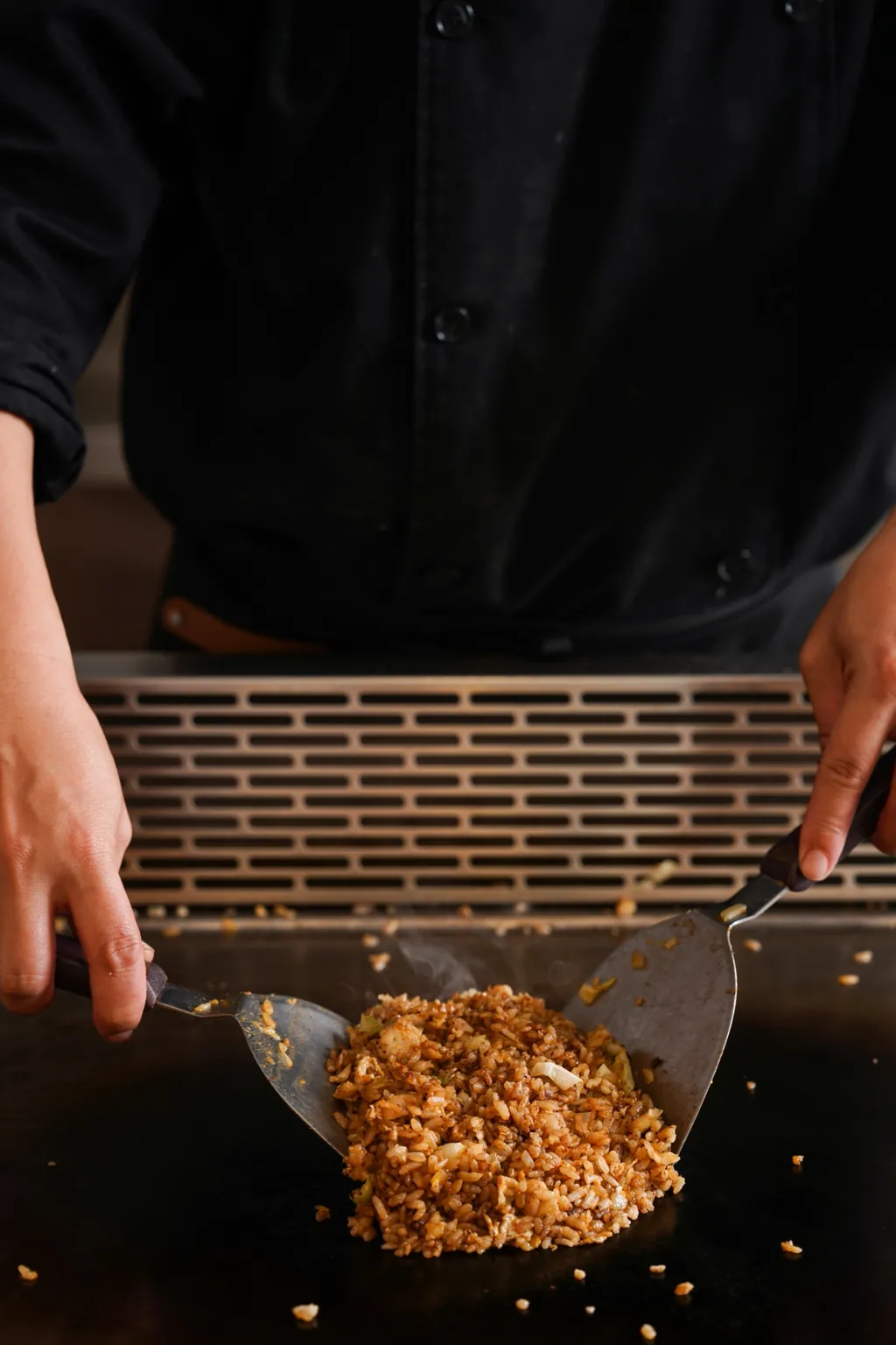 主廚雙手各持一把鏟子，在鐵板上交錯翻撥米飯